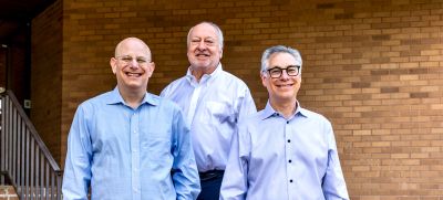 A group photo of three smiling professionals, wearing casual business attire, representing a prominent Memphis corporate real estate firm, posed on outdoor brick steps.