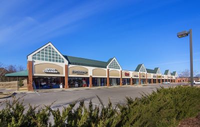 Single-story commercial shopping center with green roof accents, brick pillars, and retail storefronts including Dryve Cleaners and Papa Murphy's.