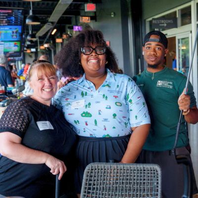 Three smiling team members enjoying a group outing at Topgolf, representing a Memphis corporate real estate company.