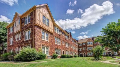 Three-story historic brick Tudor-style apartment building with green lawn in Midtown memphis