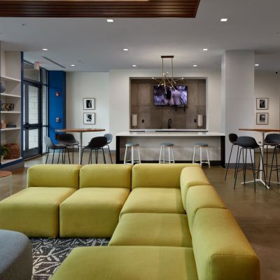 modern apartment clubhouse interior with green modular sofa, bar stools, and community tables