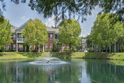 Lush green lawn and pond fountain framed by trees and brick apartment buildings at Westbury Apartments